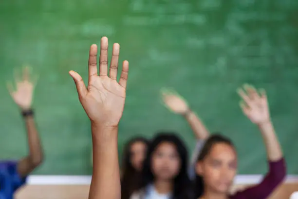 A group of people raising their hands in front of a chalkboard.