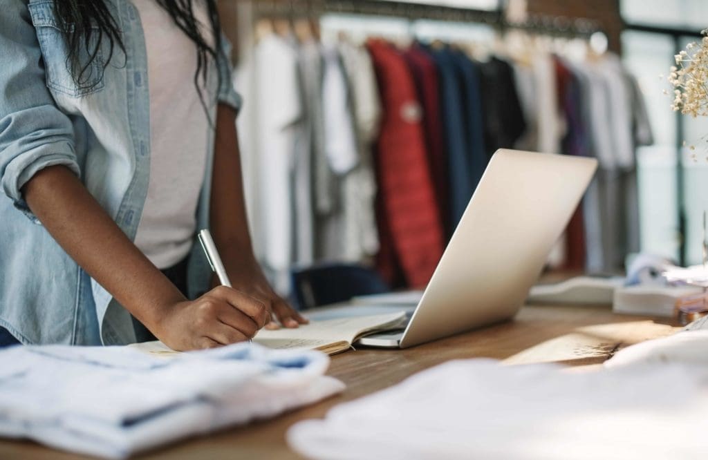 A person is working on a laptop in front of some clothes.