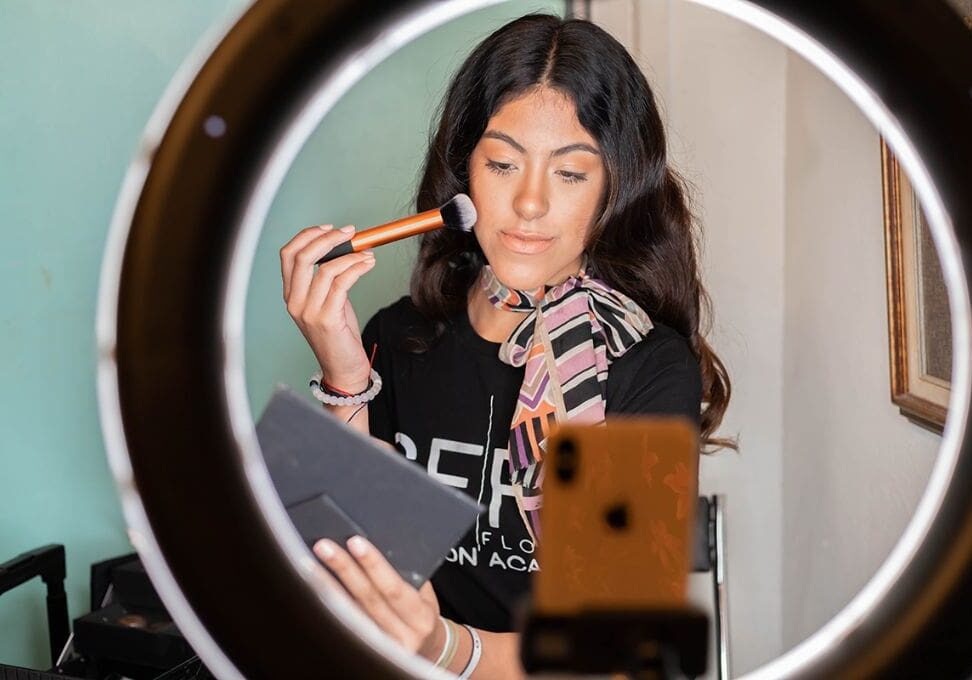 A woman is holding a brush and looking at her makeup.